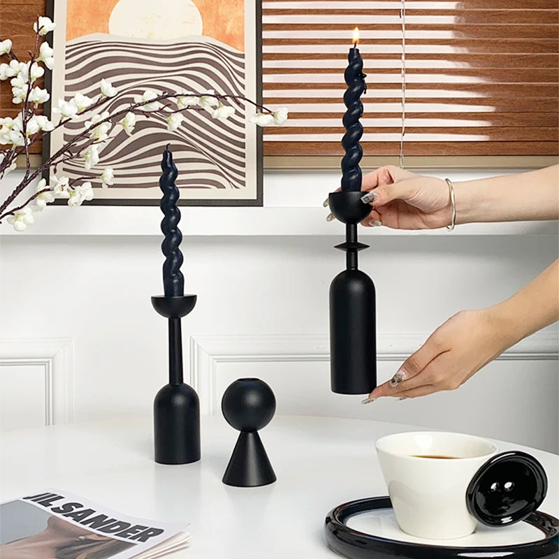 A set of two black decorative candlesticks with fluted columns and a smaller stand, displayed on a white table.