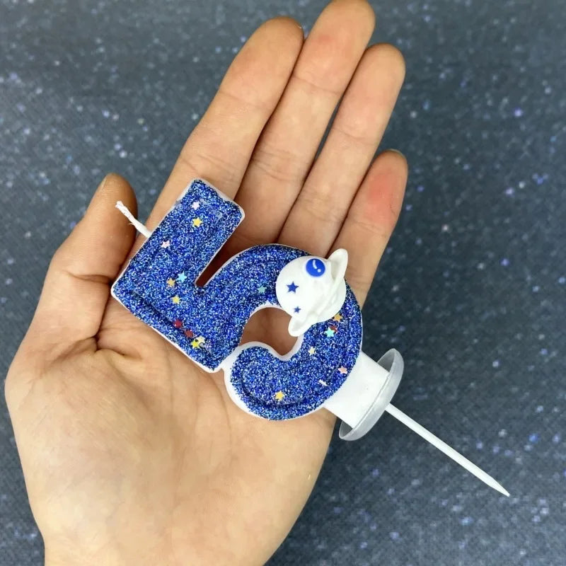 A hand holds a glittery blue number candle shaped like the number 4 with a white planet design.