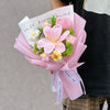 A bouquet of handmade pink crochet flowers with a handwritten note is held by a person.