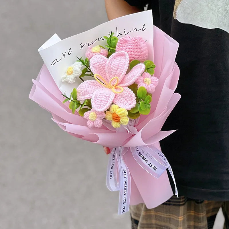 A bouquet of handmade pink crochet flowers with a handwritten note is held by a person.