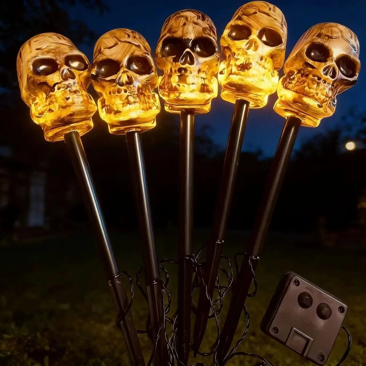 A set of glowing skull solar pathway lights mounted on dark metal stakes.