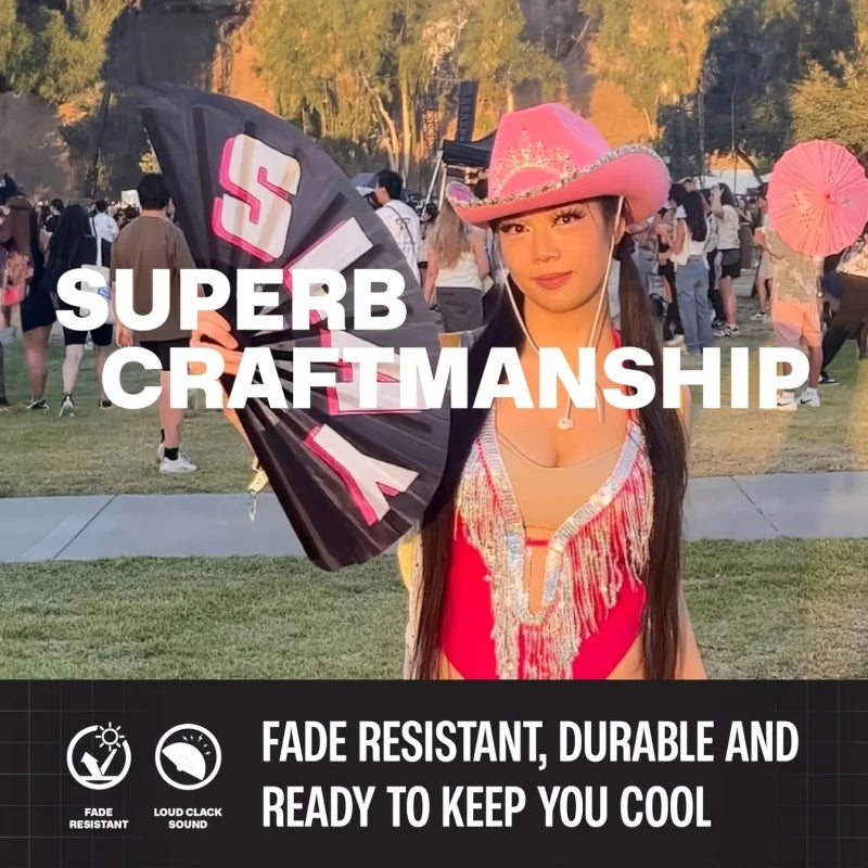 A woman wearing a pink hat and red top holds a large black foldable clapper hand fan outdoors.