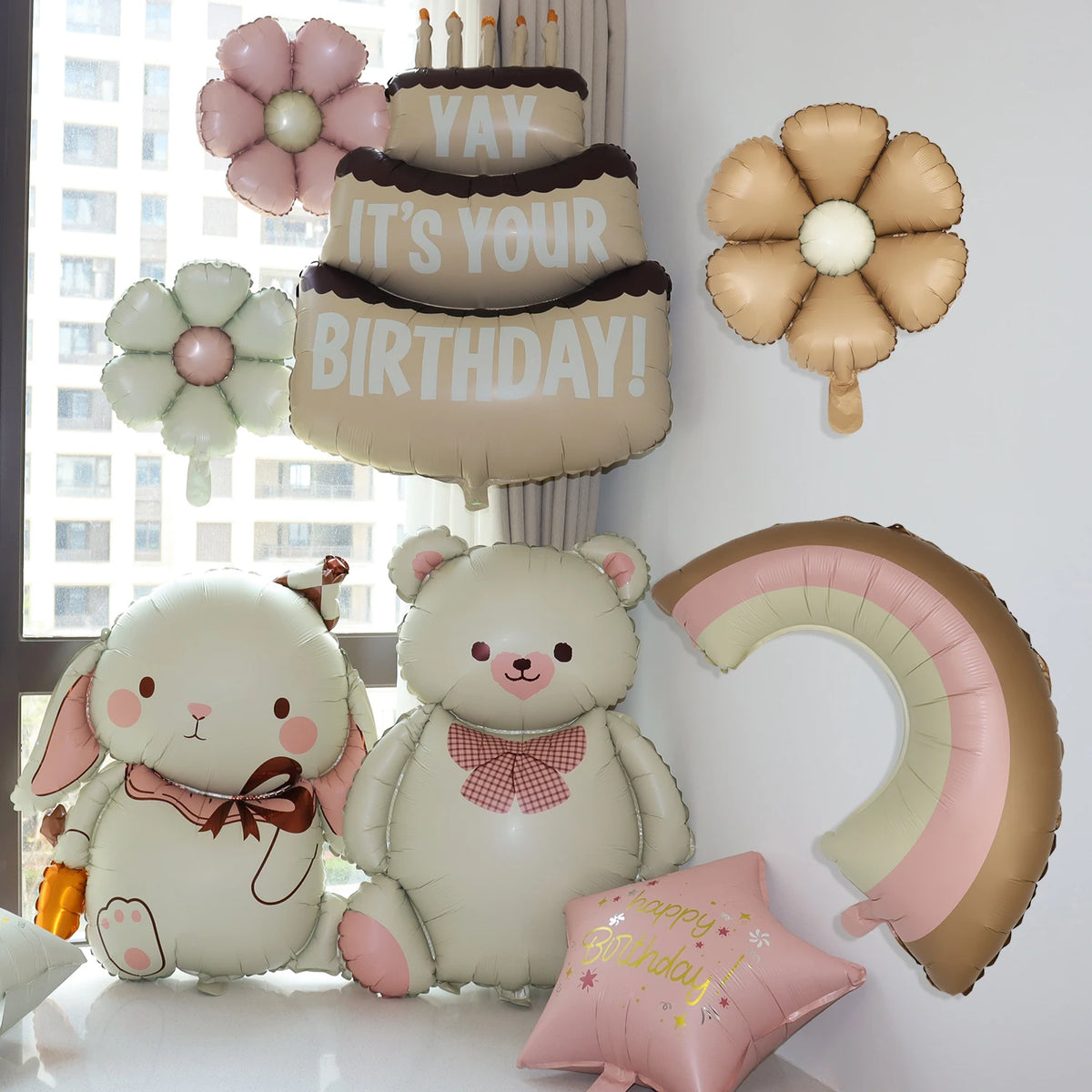 A collection of light pink and beige foil balloons, including a bear, flowers, and a birthday banner.