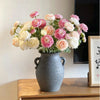 A bouquet of pink and cream silk peony flowers in a gray vase on a wooden table.