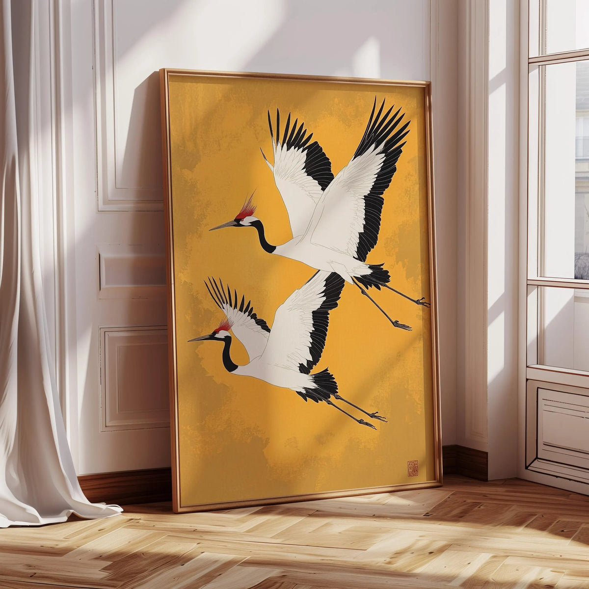 A vertical painting of two white cranes in flight on a gold canvas framed in wood.