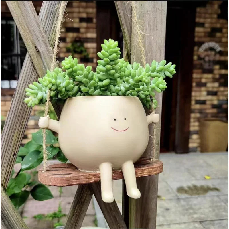 A light beige resin ornament shaped like a smiling face is hanging on a wooden trellis.