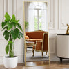 A full length body mirror with a gold frame reflecting an orange velvet sofa and interior decor.
