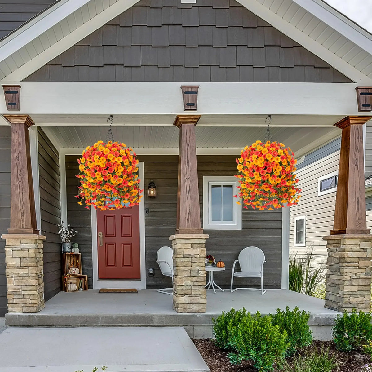 Artificial hanging morning glory flowers in vibrant orange and yellow with eucalyptus leaves displayed on a porch.