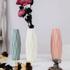 A white vase with vertical ridges stands next to a pink vase and a small gray elephant figurine.