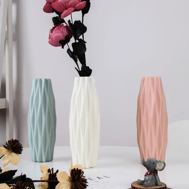 A white vase with vertical ridges stands next to a pink vase and a small gray elephant figurine.
