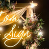 A custom neon sign featuring the words Custom Neon Sign decorated with floral arrangements against a dark background.