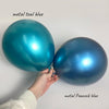 A hand is holding two metallic blue latex balloons, one teal and one peacock blue.