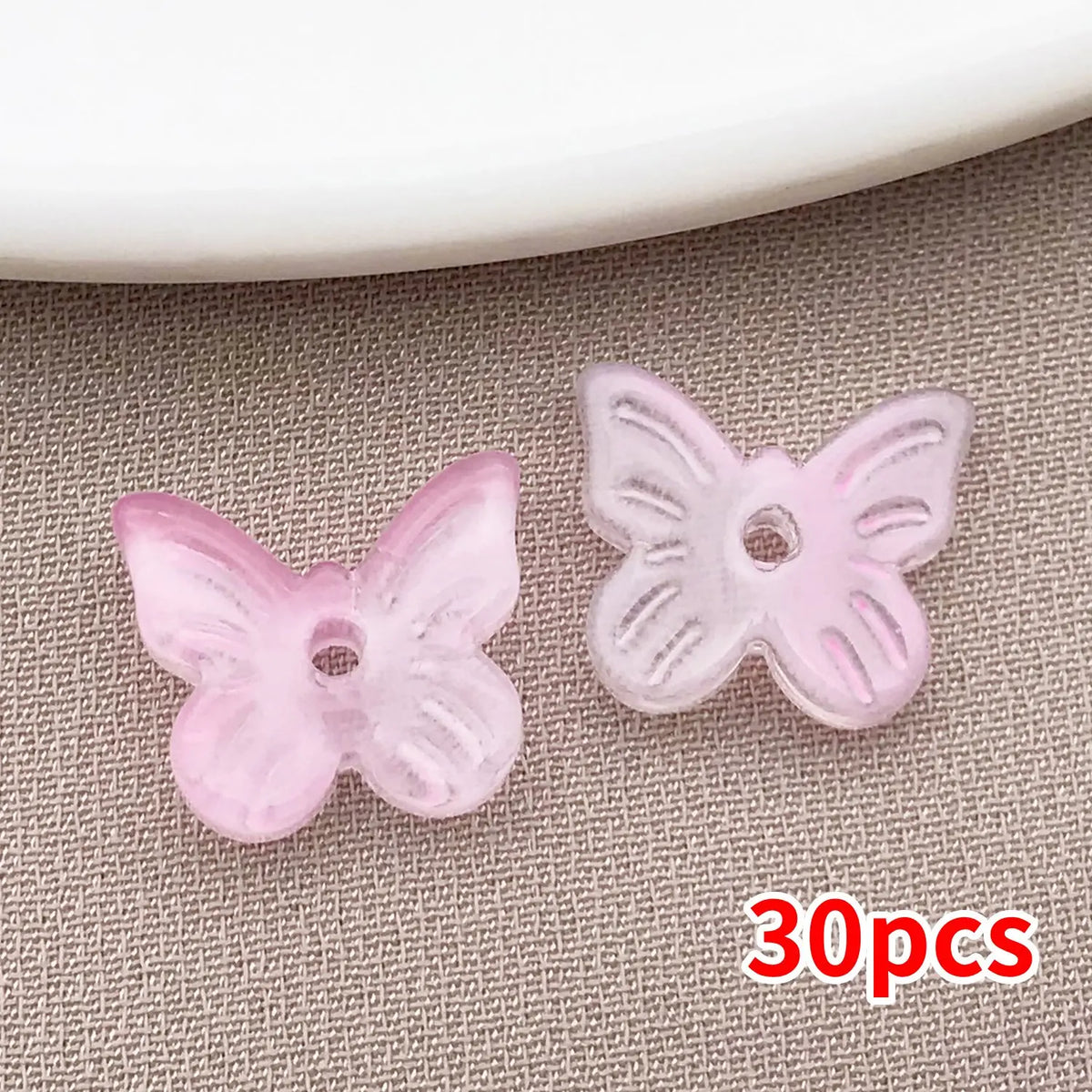 Un juego de 30 cuentas de mariposa de vidrio rosa sobre una superficie texturizada gris.