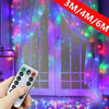 A hand holds a remote control activating fairy curtain string lights draped over a glass door.