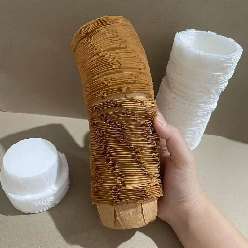 A hand holds a cylindrical paper cup made of fluted, golden-brown paper for baking or party decor.