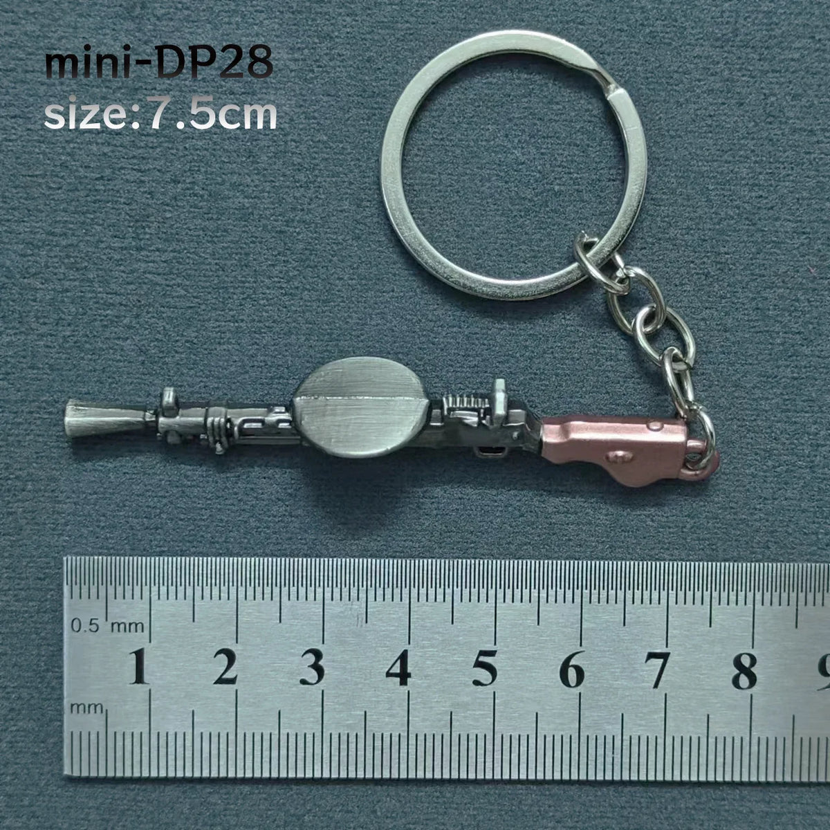 A silver alloy gun model miniature keyring with a circular barrel and a pink grip, shown next to a ruler.