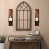 Vintage wooden wall candle holders with arched glass frames mounted on a beige wall above a wooden table.