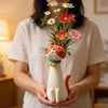 A person holds a whimsical resin cat flower vase with orange and pink flowers.