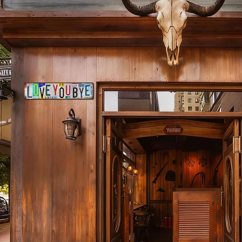 A rustic wooden door with a metal sign reading I LOVE YOU BYE and a large mounted skull above the frame.