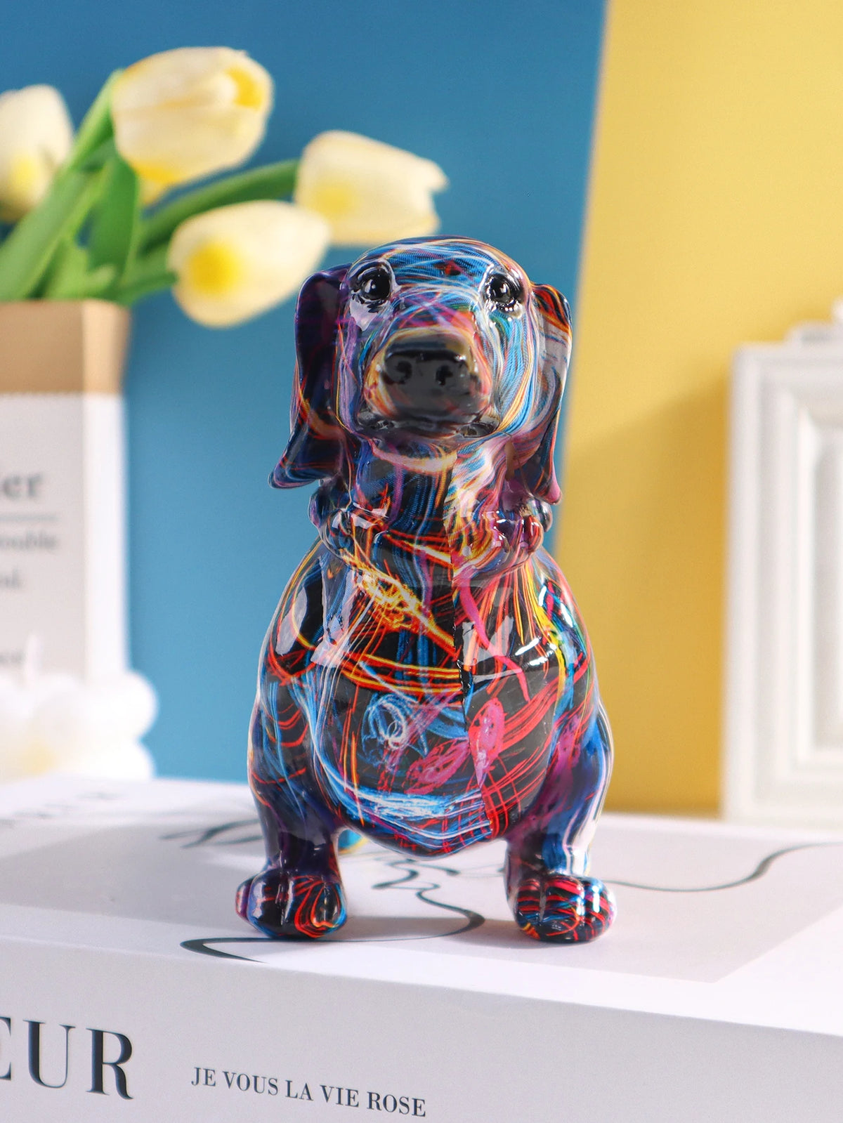 A colorful resin figurine of a dachshund dog in a sitting pose, displayed on a white box.