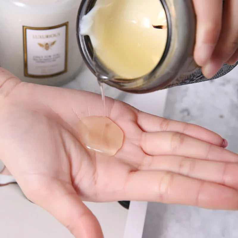A hand pours a clear wax from a glass jar into the palm of another hand for a hand-poured natural soy candle.