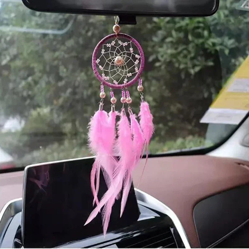 A pink feather pendant charm is displayed hanging from a rearview mirror inside a car.