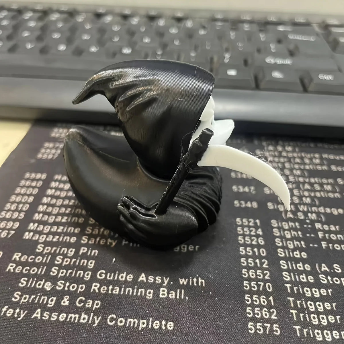 A black 3D printed Grim Reaper duck statue with a white wing, resting on a dark surface.