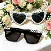 A set of black sunglasses decorated with pearl borders and 'just married' text, displayed on a white table surrounded by pink