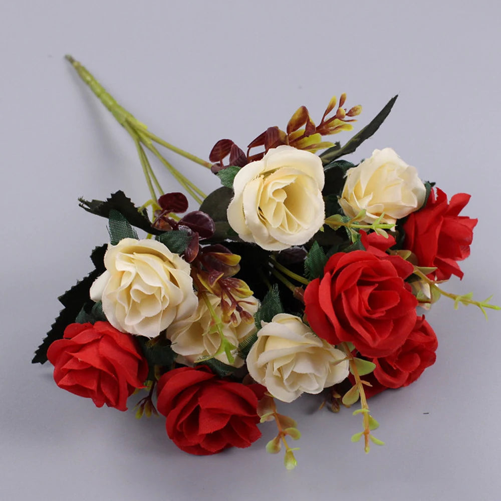 A bouquet of artificial silk roses in shades of cream and deep red with dark green foliage.