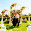 Braut und Bräutigam stehen unter einem eleganten goldenen Bogen mit Blumen und Stoffdrapierung für ein Hochzeitsfoto.