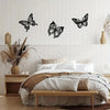 A bedroom wall decorated with three black metal butterfly silhouette art pieces above a white wooden bed.