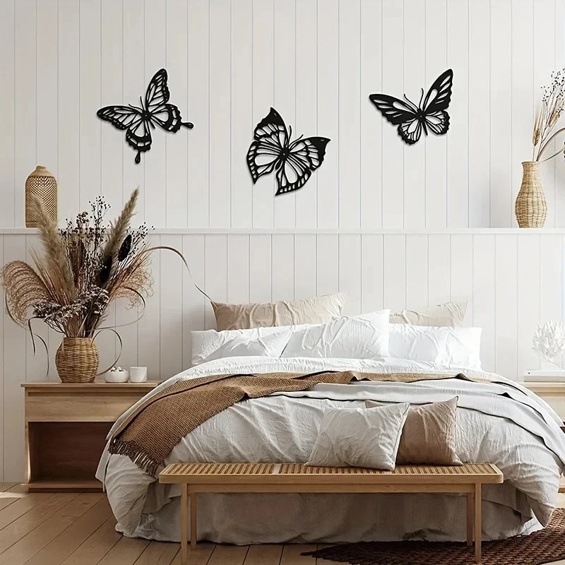 A bedroom wall decorated with three black metal butterfly silhouette art pieces above a white wooden bed.