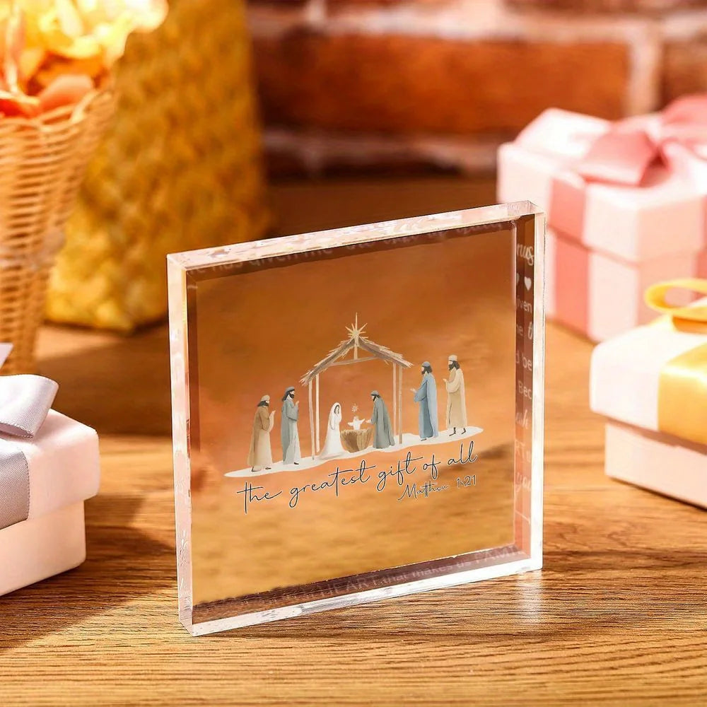 A clear acrylic nativity scene ornament featuring figures in muted colors resting on a wooden surface.