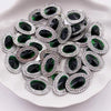 A pile of green and black gemstone flatback rhinestones with silver-toned settings on a white plate.