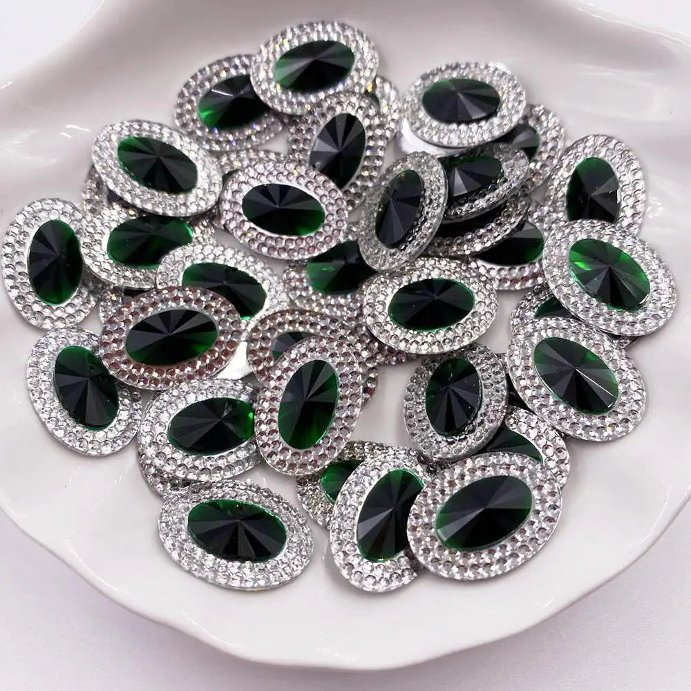 A pile of green and black gemstone flatback rhinestones with silver-toned settings on a white plate.