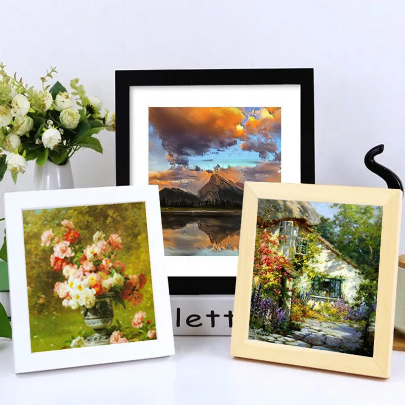 A rustic wood photo frame with a landscape painting is displayed next to a black framed print.