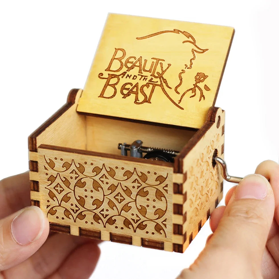 A carved wooden music box with a lid featuring the text Beauty and the Beast is held in a hand.