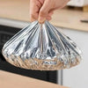 A hand is holding a reusable aluminum foil bowl cover, which is shaped like a cone for heat retention.