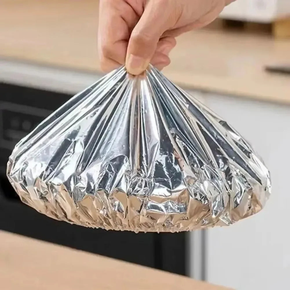 A hand is holding a reusable aluminum foil bowl cover, which is shaped like a cone for heat retention.