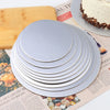 A stack of silver coated round cake boards is shown next to a wooden cutting board and printed paper.