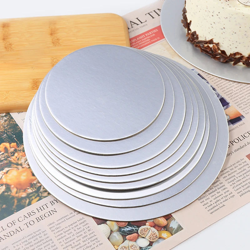 A stack of silver coated round cake boards is shown next to a wooden cutting board and printed paper.