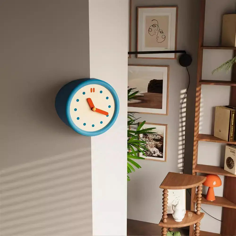 A modern resin wall clock with a blue face and orange hands is mounted on a light gray wall.