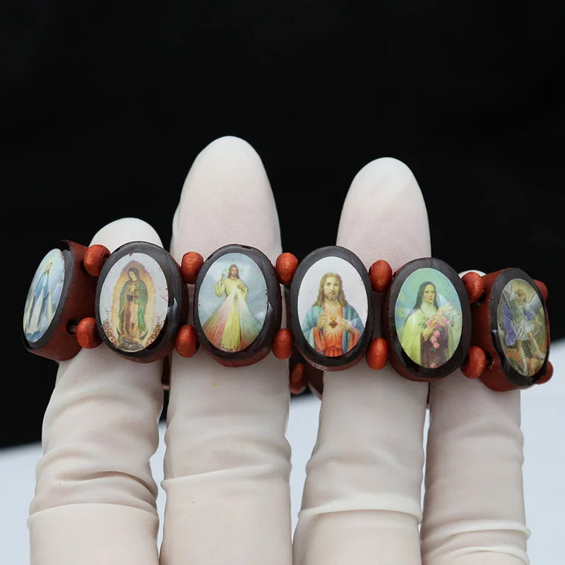 A hand displays a natural wooden rosary bracelet featuring charms of the Virgin Mary and Jesus.
