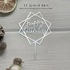 A silver acrylic birthday topper with a geometric design and the words happy birthday on a wooden surface.