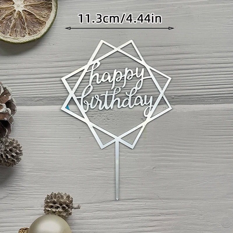 A silver acrylic birthday topper with a geometric design and the words happy birthday on a wooden surface.