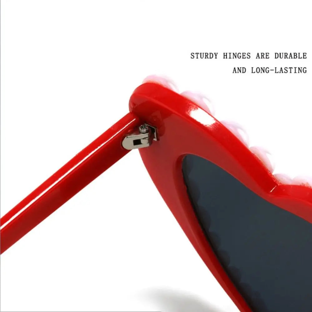 Close-up of red heart-shaped sunglasses showing sturdy hinges and a dark lens.