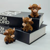 A set of three cute brown Highland cow statues displayed on stacked black books.