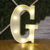 A glowing white alphabet letter G made of LED lights resting on a wooden surface.