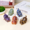 A collection of natural crystal cat statues in various colors including green, blue, purple, and amber on a white surface.