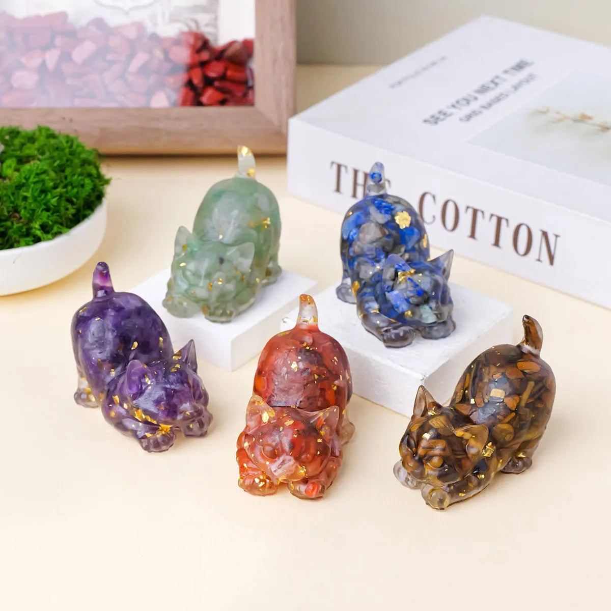A collection of natural crystal cat statues in various colors including green, blue, purple, and amber on a white surface.